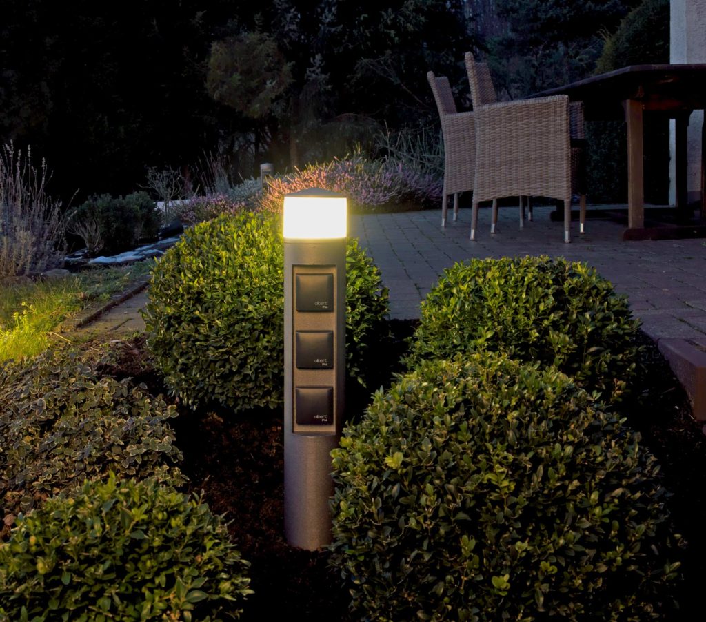 Eine Steckdosensäule mit integrierter Leuchte steht in einem Terrassenbeet