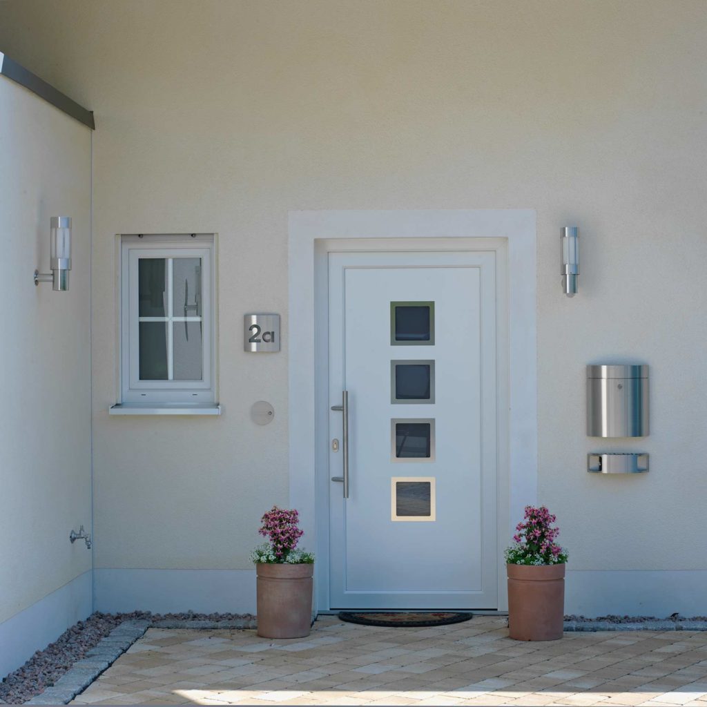Ein weiß gestrichener Hauseingang mit Blumenkübeln, Hausnummer und Außenleuchten