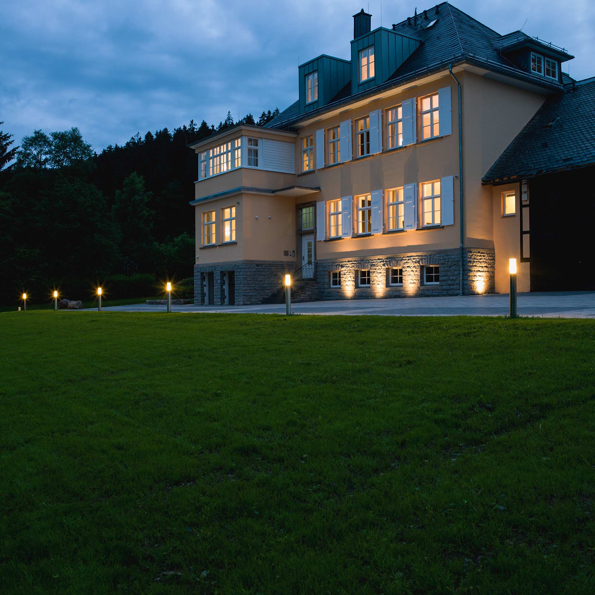 Ein großes Gutshaus wird durch mehrere Außenleuchten in der Abenddämmerung erhellt