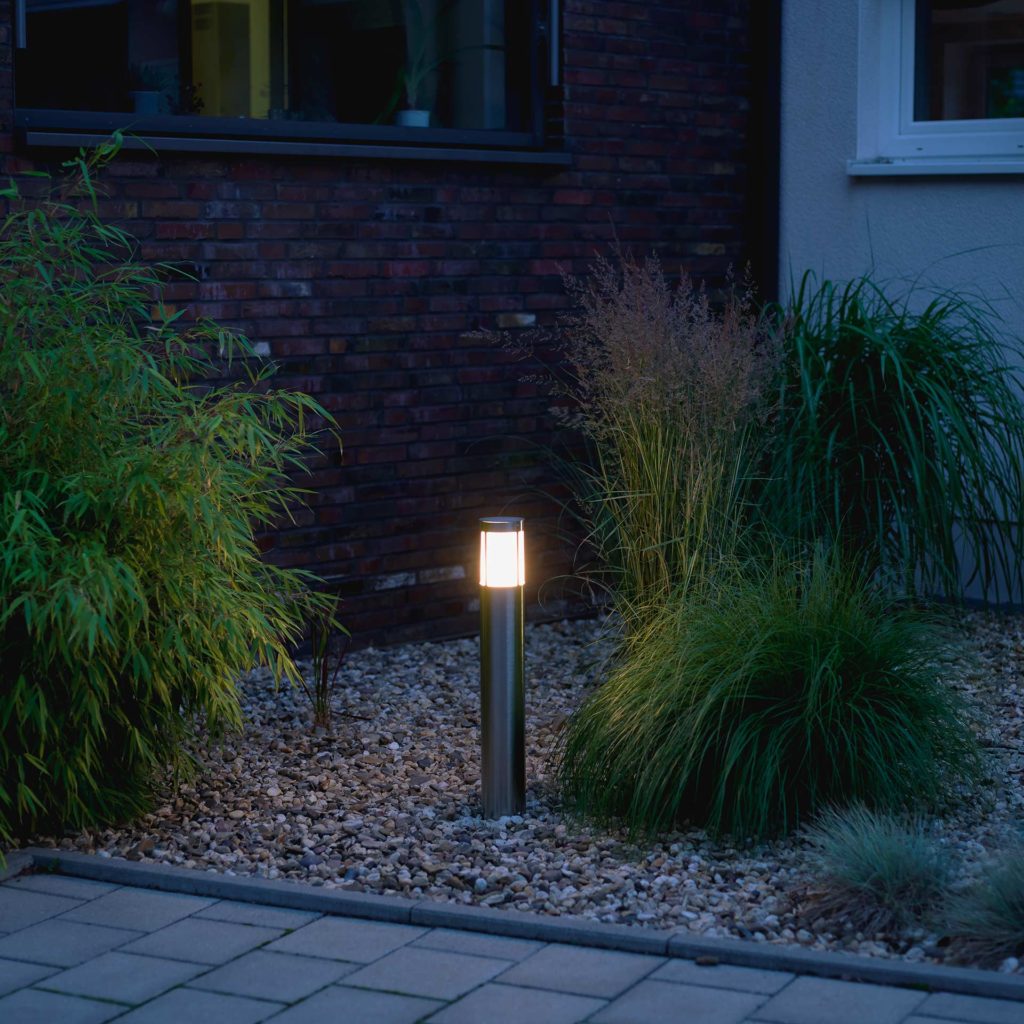 A bollard light illuminates a bed with plants.