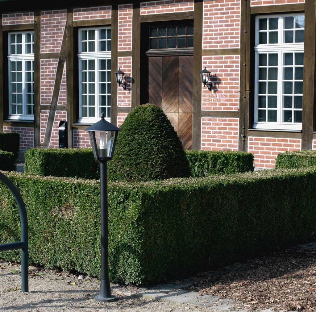 Eine Gartenanlage mit Hecke, Büschen und mittelhohen Lichtmasten