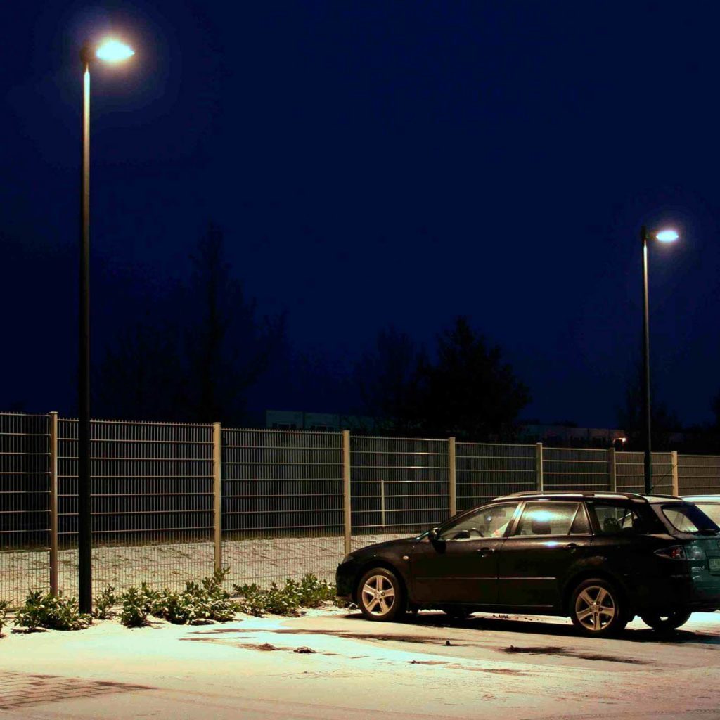 Tall and modern pole lights stand on the edge of a parking lot.