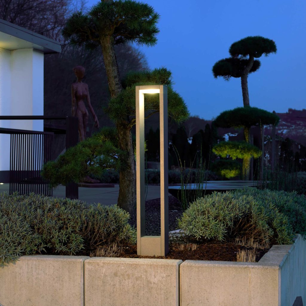 A modern light column illuminates a garden area.