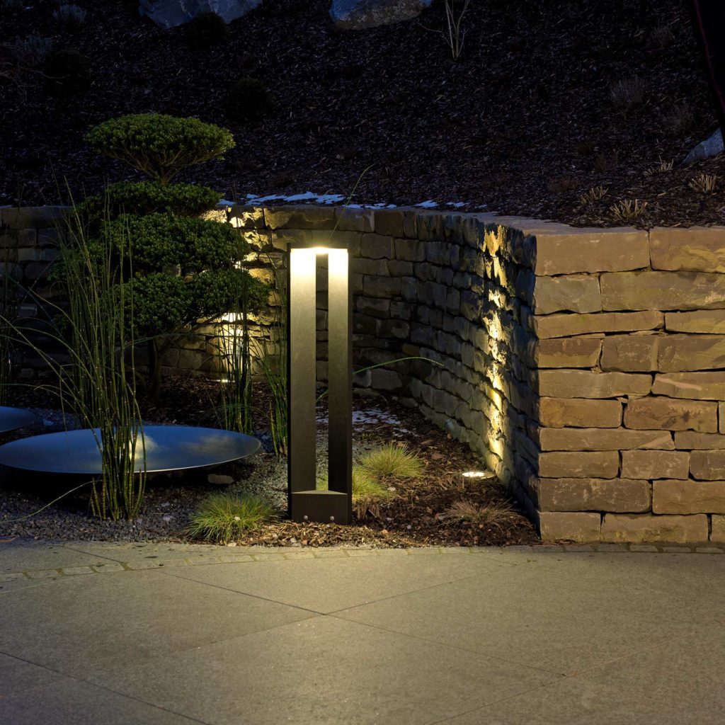 A modern path light provides cozy light on an old stone wall.