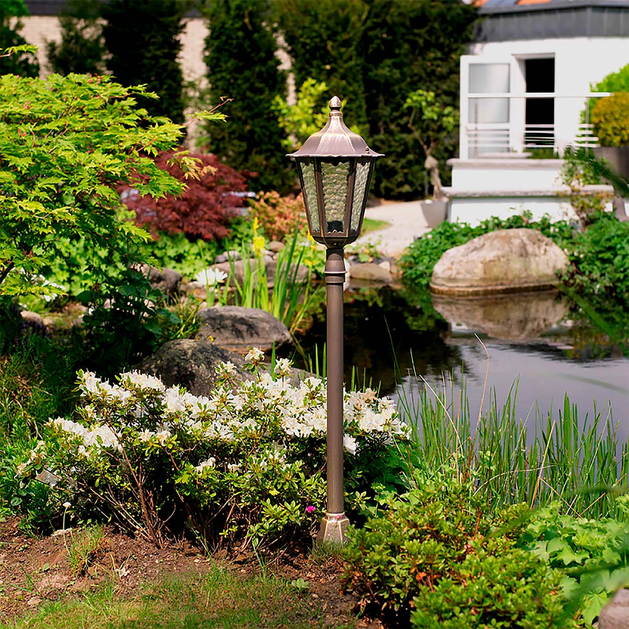 Eine klassisch anmutende Außenleuchte steht an einem begrünten Gartenteich