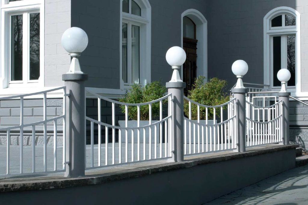 A wrought iron garden fence of high quality, on which pedestal lights are enthroned