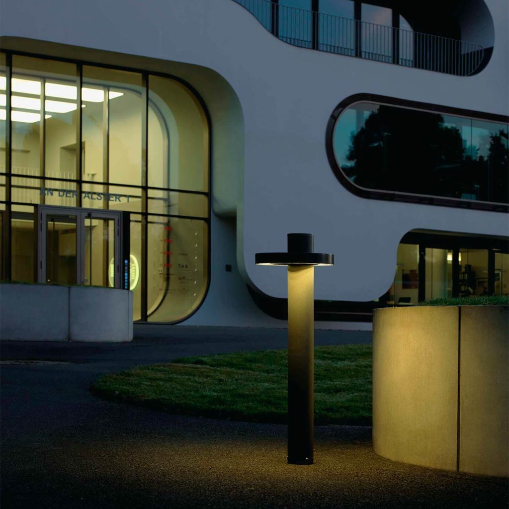 A stylish object lighting stands by a large office building.