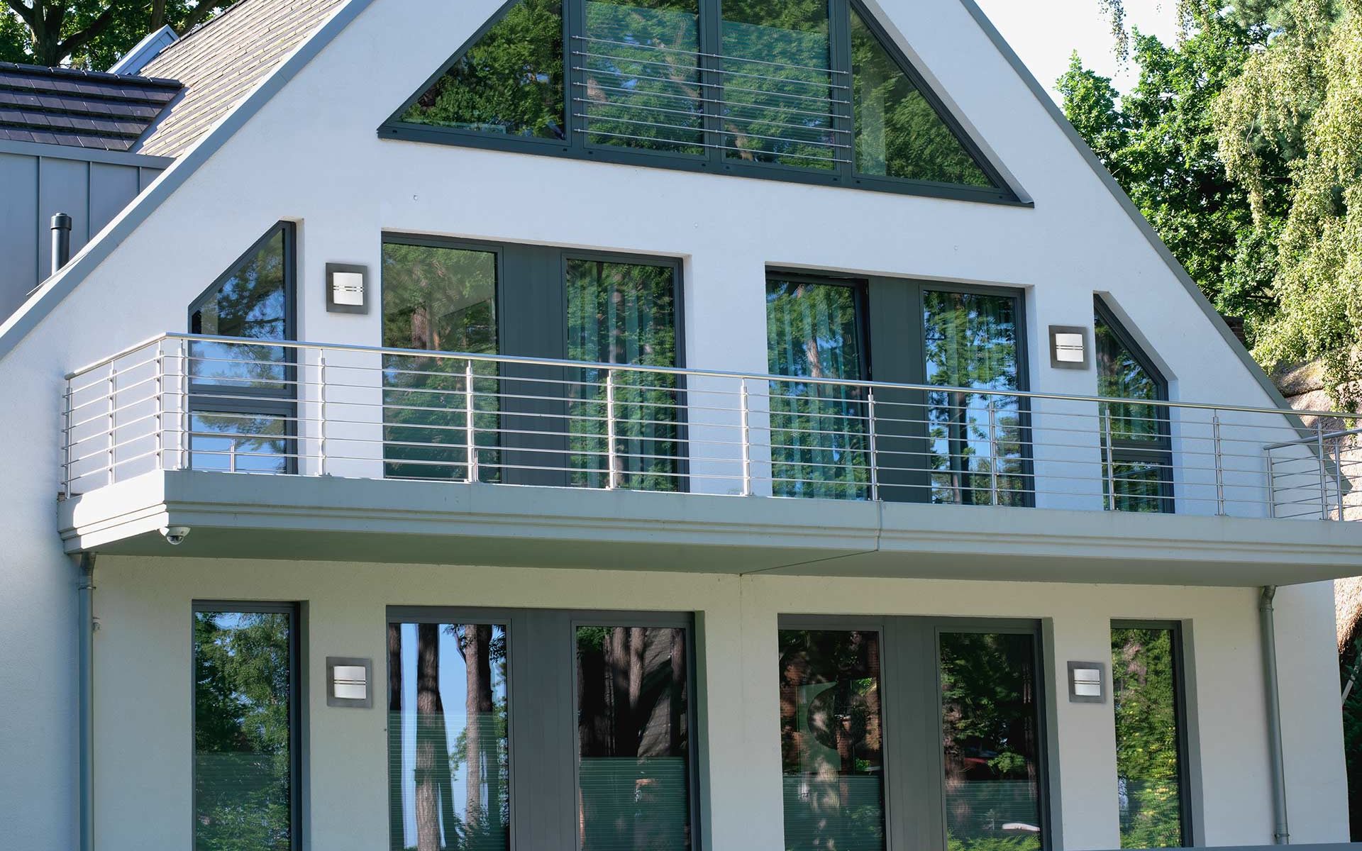 Ein modernes Haus mit Balkon und vier geometrisch angeordneten Wandleuchten.