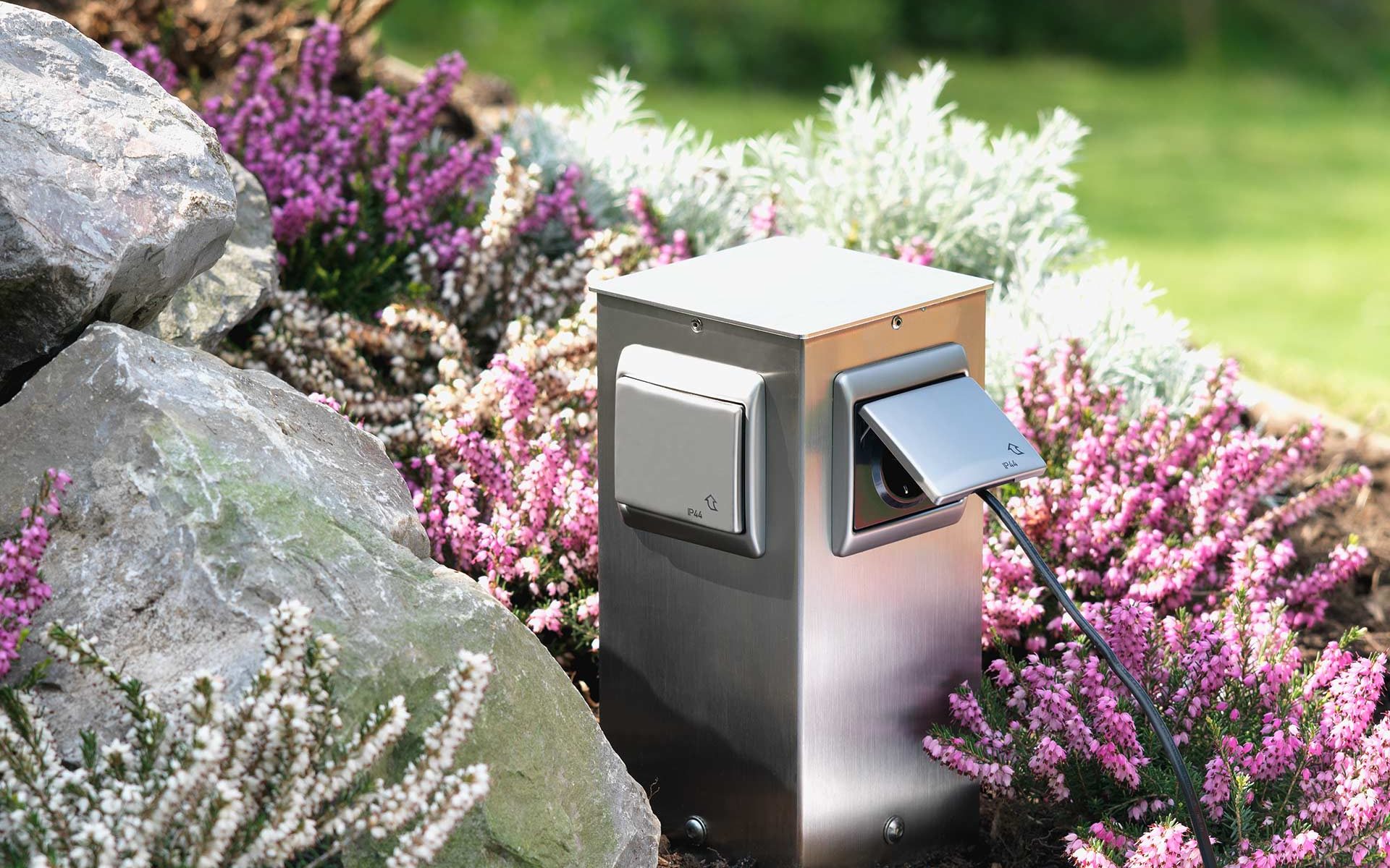 An inconspicuous stainless steel socket column provides power in a flowerbed.