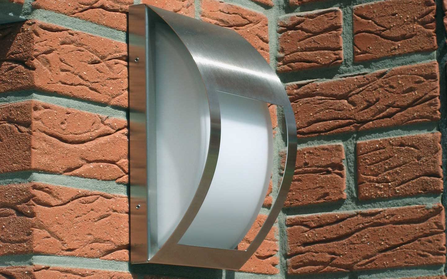 Close-up of a modern stainless steel wall lamp at a house entrance.