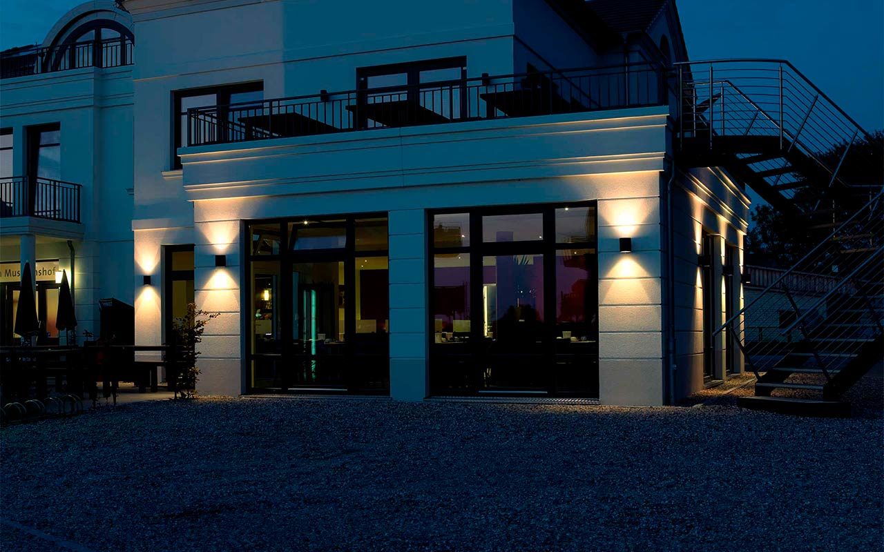 A multi-storey villa is stylishly illuminated by two wall lights at dusk.