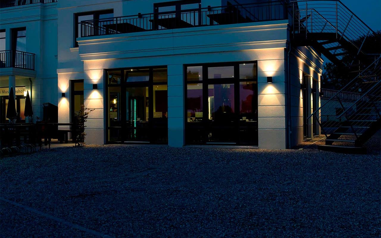 Eine mehrstöckige Villa wird in der Abenddämmerung von zwei Wandleuchten stilvoll beleuchtet.

